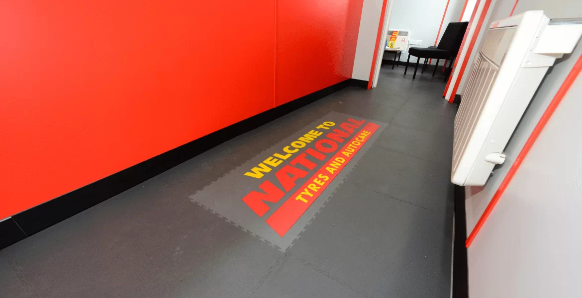 Interlocking floor tiles in the reception of a National tyres garage, featuring a branded welcome to National Tyres logo printed onto the floor tiles