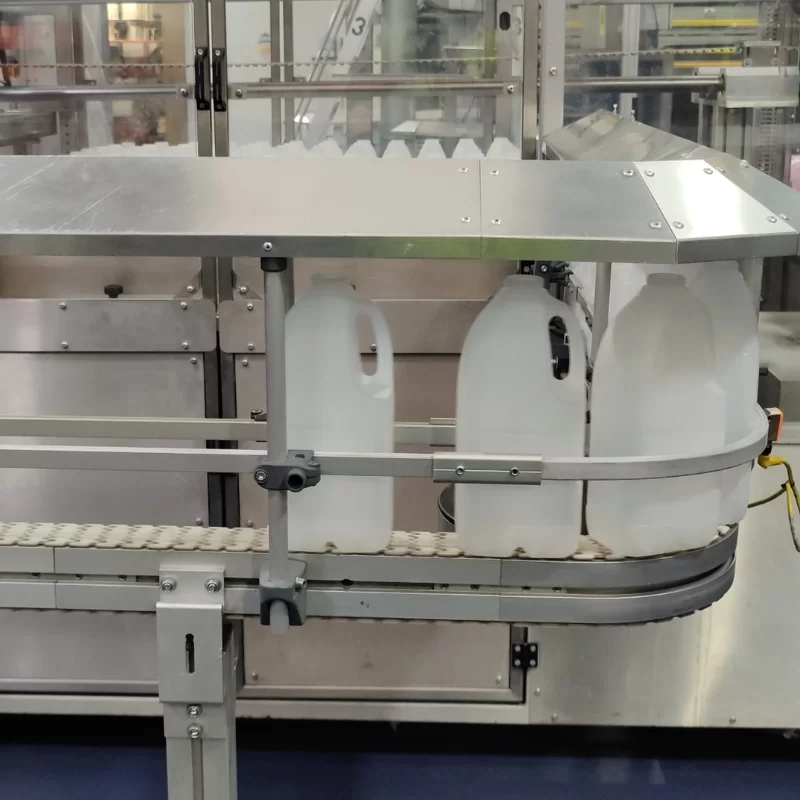 Milk bottles on a production conveyor with blue ecotile flooring underneath the manufacturing machinery