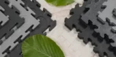 A range of Ecotile recycled interlocking floor tiles on a bare concrete floor with green leaves signifying sustainability and green credentials of the product