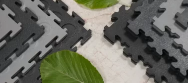 A range of Ecotile recycled interlocking floor tiles on a bare concrete floor with green leaves signifying sustainability and green credentials of the product