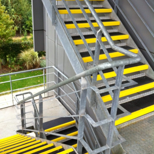 „Suregrip“-Treppenstufenbeläge auf den Außentreppen, die das Treppenhaus hinunterführen, in Schwarz mit gelben Kanten an jeder Stufe