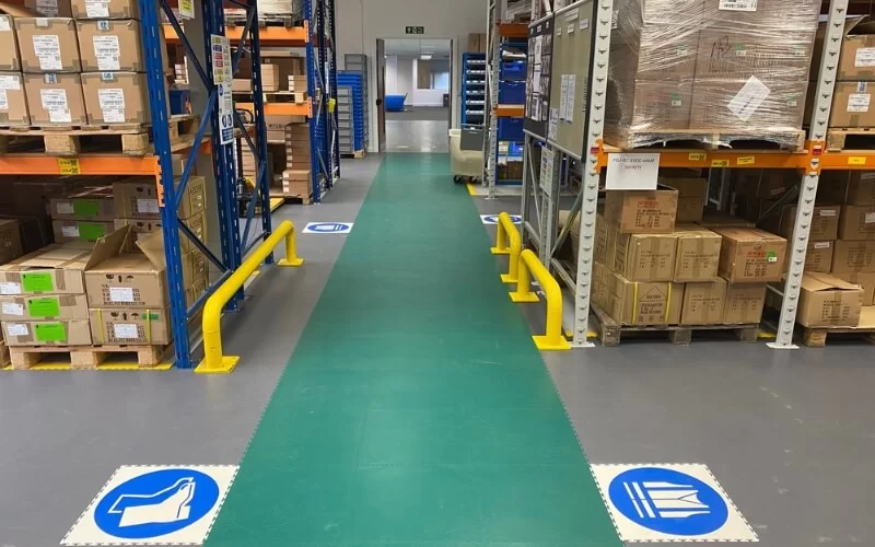Green ecotile floor tiles used to create a safe walkway through a warehouse, with accompanying safety logo floor tiles for safety boots and hi-vis requirements