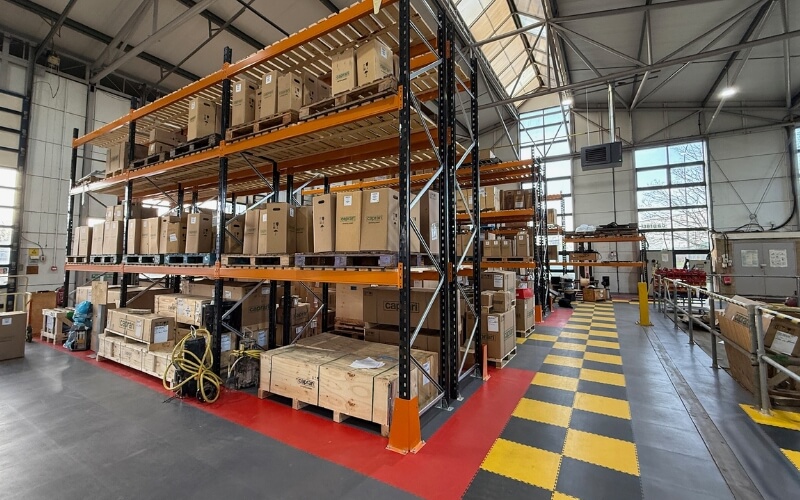 Regale von Bradfield Storage Handling in einem Lager, das mit einem „Ecotile“-Industrieboden ausgelegt ist, mit sicheren Laufwegen und durch verschiedenfarbige, ineinandergreifende Bodenfliesen abgegrenzten Bereichen
