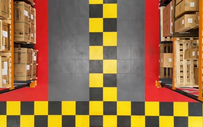 Bright ecotile floor tiles on a warehouse flooring, shot from above the racking, with red tiles around the racking, combined with graphite floor tiles and a black and yellow checkered walkway