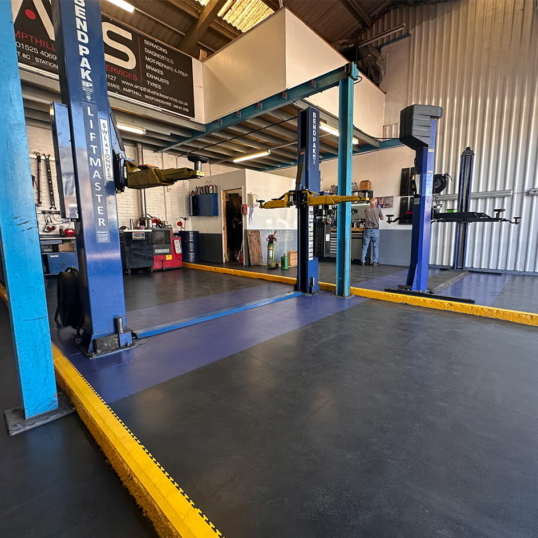 Ecotile graphite and blue tiles in car lift bay, with yellow ramps to signify safety markings