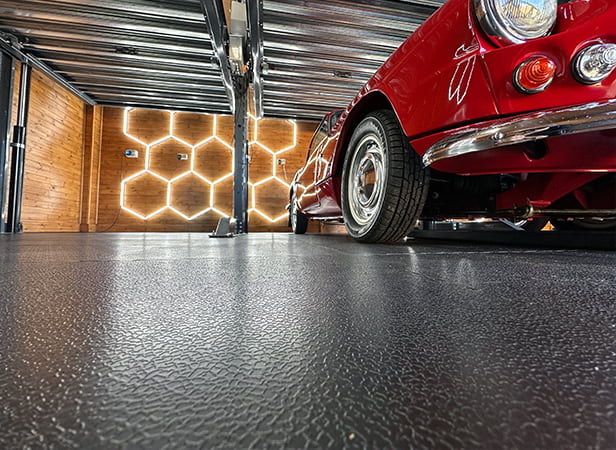 Close up showing a red car, with HEX lighting and a garage lift, on ecotile workshop floor tiles