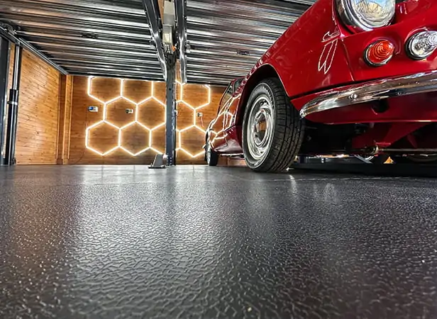 Close up showing a red car, with HEX lighting and a garage lift, on ecotile workshop floor tiles
