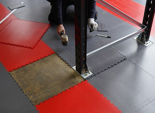 Image showing Ecotile's warehouse floor tiles being installed around the foot of warehouse racking, showing how they are cut.