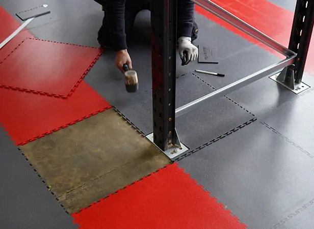Image showing Ecotile's warehouse floor tiles being installed around the foot of warehouse racking, showing how they are cut.