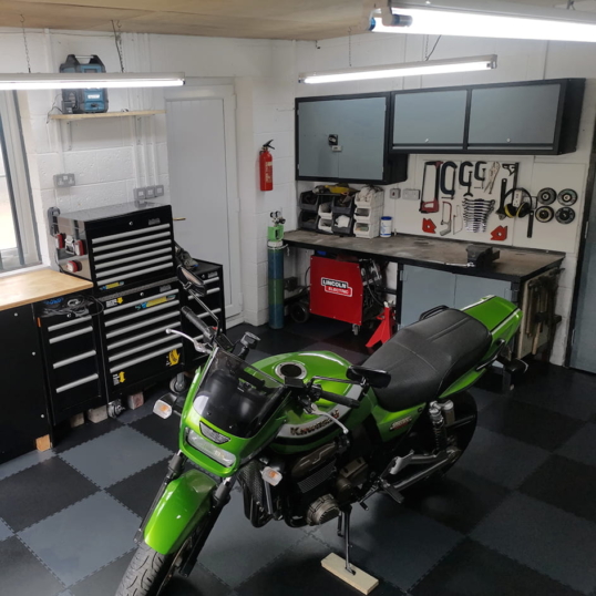 Une image représentant une moto verte sur un revêtement de sol de garage en PVC, avec un motif gris foncé et noir