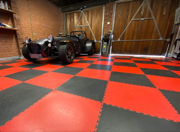 Image prise en contre-plongée d'un sol de garage à carreaux rouges et noirs, sur lequel se trouve un véhicule