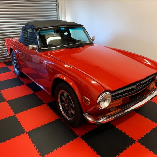 Une photo d'une voiture de collection rouge vif posée sur le sol d'un garage à carreaux rouges et noirs