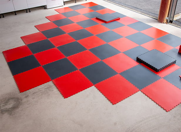 Image montrant la pose de dalles de sol de garage emboîtables, rouges et grises, sur un sol en béton